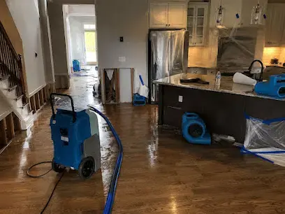 A kitchen with a dehumidifier and air movers drying the wood floor and lower cabinets