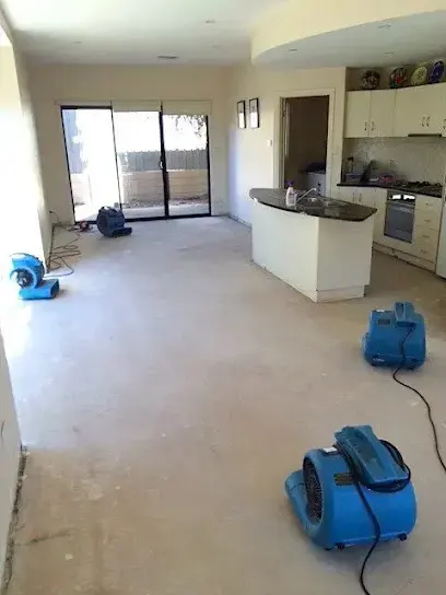 Blue air movers drying a bare floor in an open Imperial Beach living area with a kitchen island