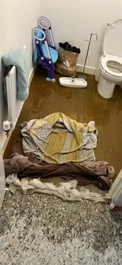 A bathroom floor covered in brown sewage water around towels after a toilet backup