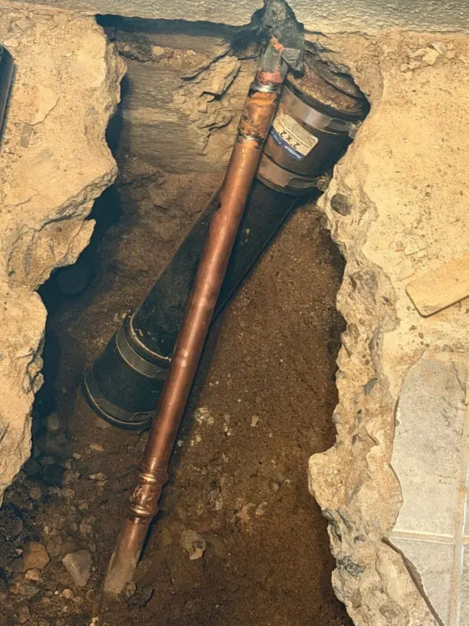A copper supply pipe exposed in a trench cut through a concrete slab floor