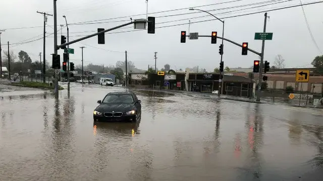 A car driving through a flooded intersection during a heavy winter rainstorm in Southern California