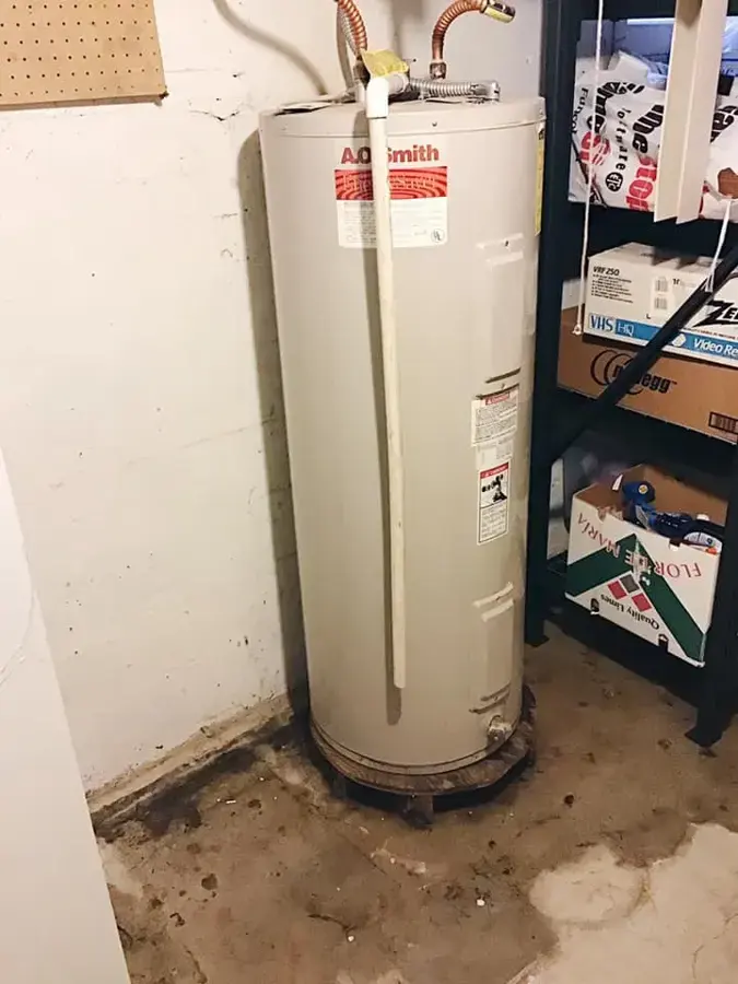 A tank water heater with water and stains spread across the floor around it